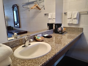 A bathroom with a granite countertop, a white sink, a mirror, a towel rack, and a coffee maker. - University Inn (Corvallis)