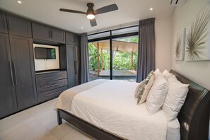 A bedroom with a bed, a TV, and a view of greenery outside.