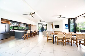 A modern kitchen with a central island, dining area with wooden chairs, and ceiling fans.