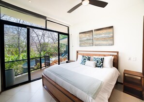 A bedroom with a large bed, a ceiling fan, and a view of a garden and pool through floor-to-ceiling windows. - Tamarindo, Senderos Gated Community Oasis. (Tamarindo)