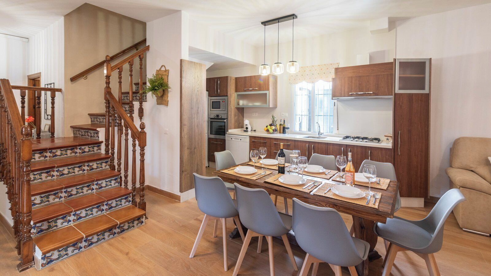 A modern kitchen with wooden cabinets, a dining table set for six, and a staircase with ornate railings.