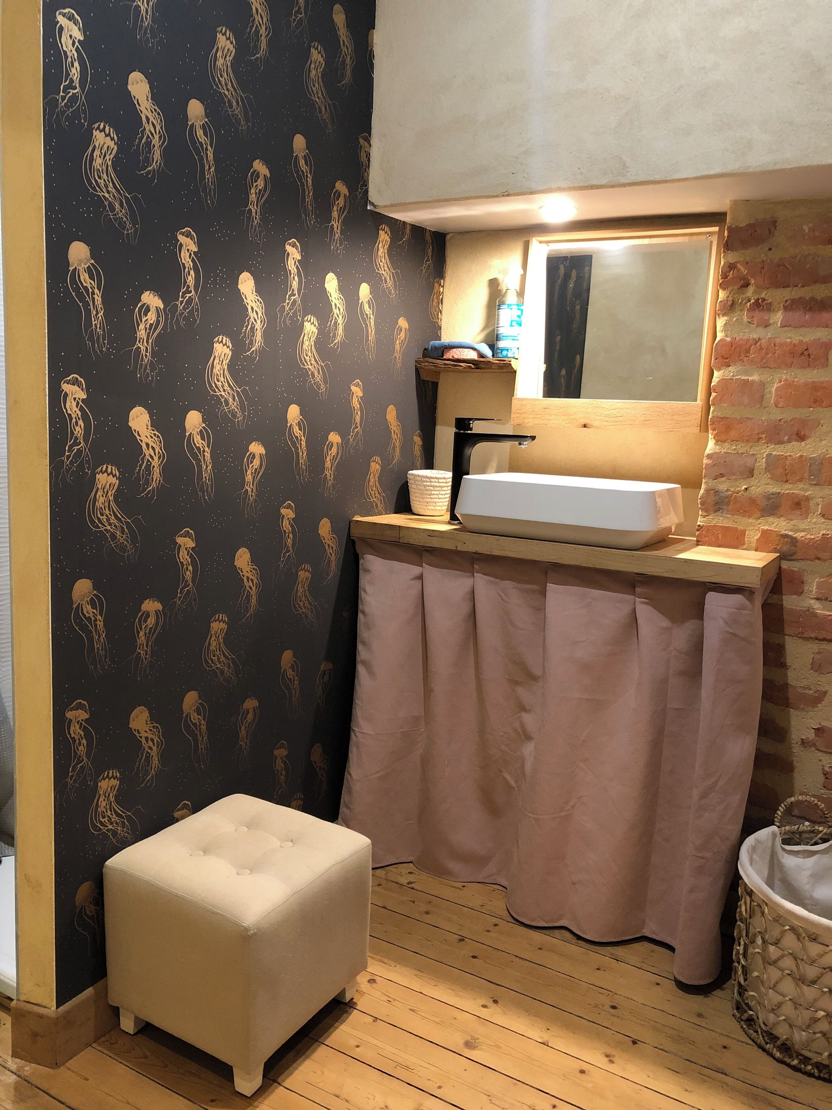 A bathroom with a black wall featuring a jellyfish pattern, a white sink, a wooden stool, and a pink curtain.