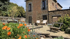 A stone building with a chimney, a wooden deck, and outdoor seating. - For a vacation in the heart of the magic of Brocéliande, come and stay at Le Libert (Mauron)
