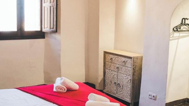 Una habitación de hotel con una cama, una colcha roja y toallas dobladas con cuidado.