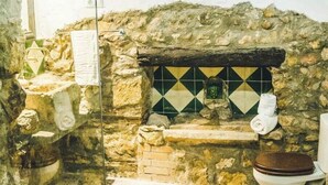 Un baño con pared de piedra, lavamanos con azulejos y un inodoro con asiento de madera.