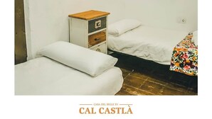 Una habitación pequeña y sencilla con dos camas, una mesita de noche de madera y una lámpara fijada a la pared.