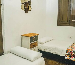 Une petite pièce simple, avec deux lits, une table de chevet en bois et un luminaire fixé au mur.