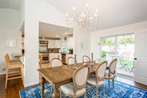 A dining area with a wooden table and chairs, a chandelier, and a view of the kitchen and outdoor patio.