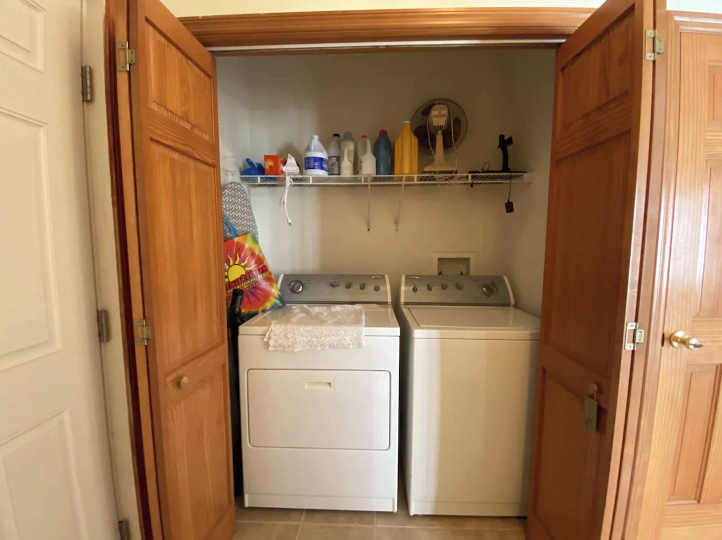Un espace buanderie avec deux machines à laver blanches et une étagère au-dessus contenant des produits de nettoyage.