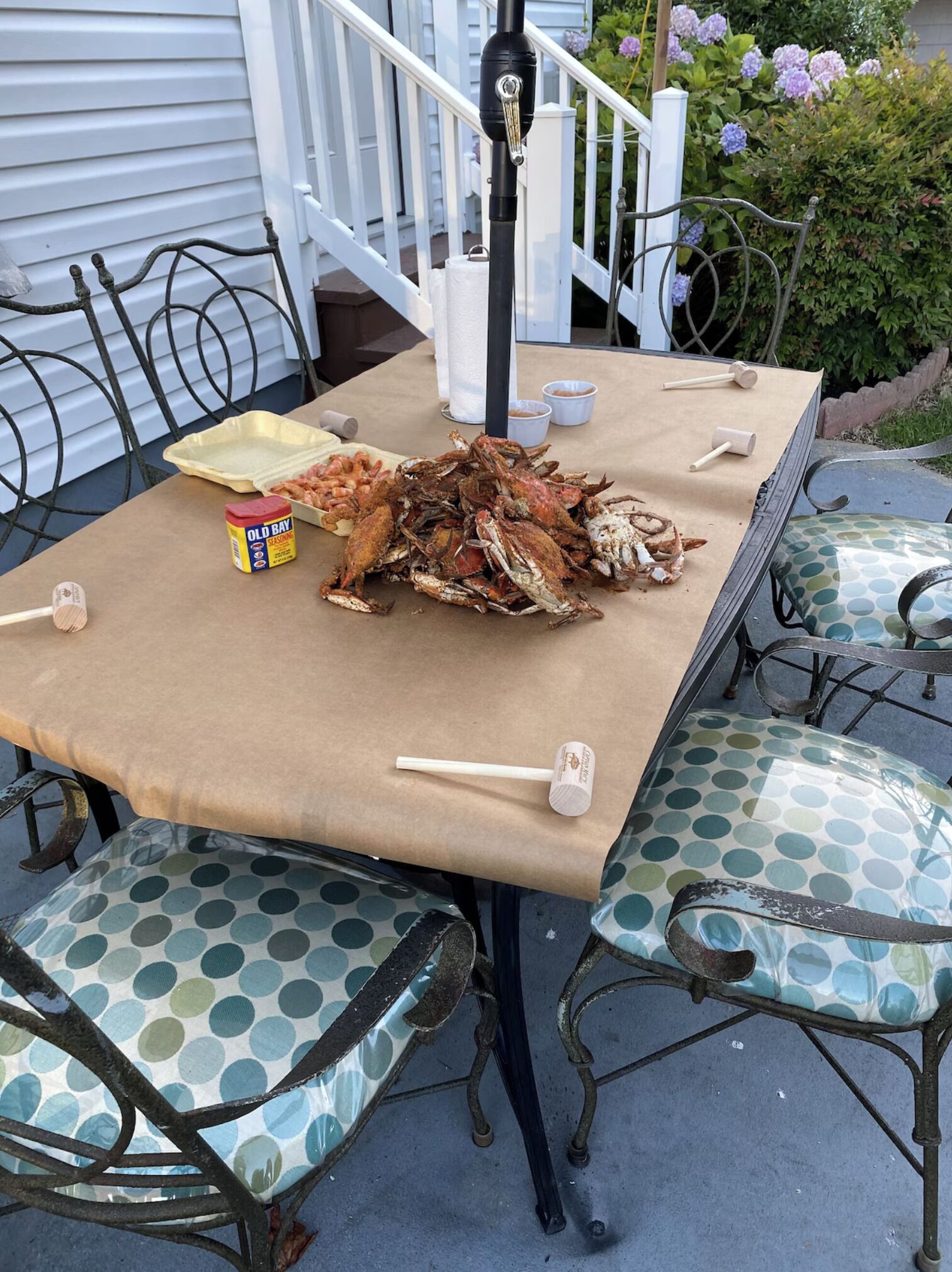 A table set outdoors with a large pile of crabs, a container of Old Bay seasoning, and wooden mallets.