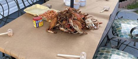 A table set outdoors with a large pile of crabs, a container of Old Bay seasoning, and wooden mallets.