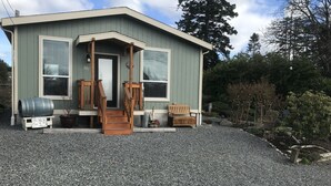 A small, single-story building with a front porch, a wooden bench, and a barrel. - Cooper's Cottage (Camano)