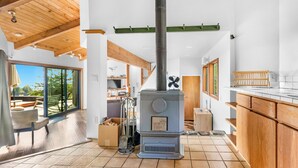 A modern kitchen with a wood-burning stove, large windows, and a view of the outdoors. - Panoramic Ocean Views, Hot Tub Under The Stars and EV charging station  (Sea Ranch)