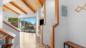A modern interior with wooden beams, a bench, a TV, and a sliding glass door leading to an outdoor area. - Panoramic Ocean Views, Hot Tub Under The Stars and EV charging station  (Sea Ranch)