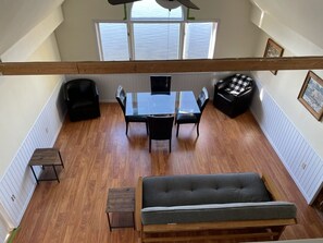 A loft-style room with a high ceiling, a dining table with chairs, a sofa, and a bench.