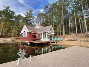 A houseboat with a covered deck and a small porch, surrounded by a forest and a body of water. - Near Munising snowmobile trails. Ride out from the property (Munising)