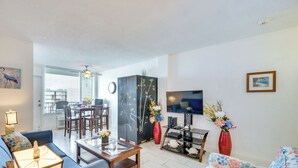 A living room with a sofa, coffee table, TV, and a dining area with chairs and a table. - Daytona Beach Condo w/ Ocean-View Balcony! (Daytona Beach)