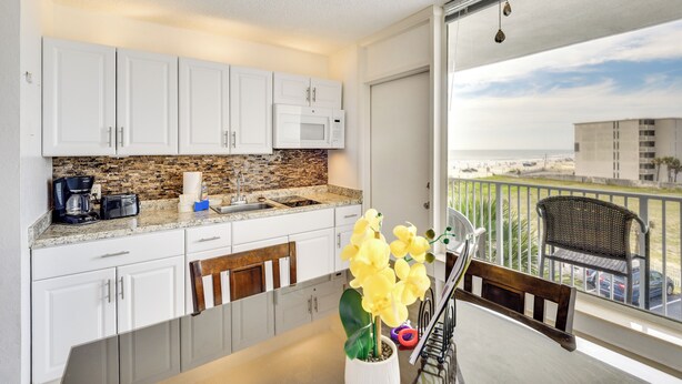 A modern kitchen with white cabinets, a granite countertop, and a view of the city through a large window. - Daytona Beach Condo w/ Ocean-View Balcony! (Daytona Beach)