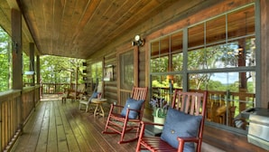 A wooden porch with rocking chairs and a table, large windows with a view of trees, and a hanging light fixture. - Stunning Mountain Cabin w/ Pool Table, Hot Tub, Wifi, 20 min to Blue Ridge (Blue Ridge)