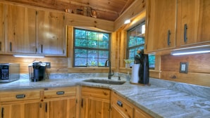 A wooden cabin kitchen with a large window, wooden cabinets, a sink, and a countertop with various appliances. - Stunning Mountain Cabin w/ Pool Table, Hot Tub, Wifi, 20 min to Blue Ridge (Blue Ridge)