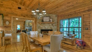 A wooden cabin interior with a dining area, fireplace, stone wall, and large windows. - Stunning Mountain Cabin w/ Pool Table, Hot Tub, Wifi, 20 min to Blue Ridge (Blue Ridge)