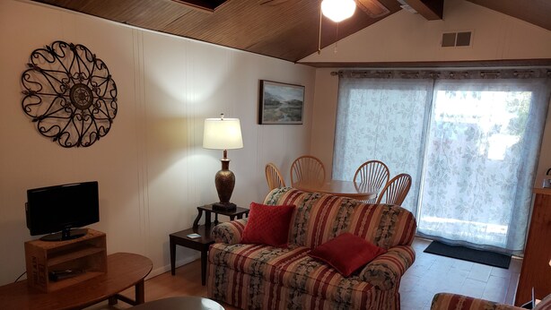 Un salon avec un canapé, un téléviseur posé sur un meuble en bois, une lampe et une table à manger avec des chaises.