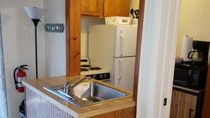Une cuisine compacte dotée d’un îlot en bois, d’un évier en acier inoxydable et d’un réfrigérateur blanc.