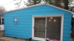 Un abri de jardin bleu orné d’une boussole, doté d’une porte coulissante en verre et de deux pots contenant des fleurs roses.