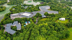 An aerial view of a large, lush green campus with multiple buildings, including a main building with a large roof and several smaller structures. - Hengshan Beijiao Hotel (Shanghai)