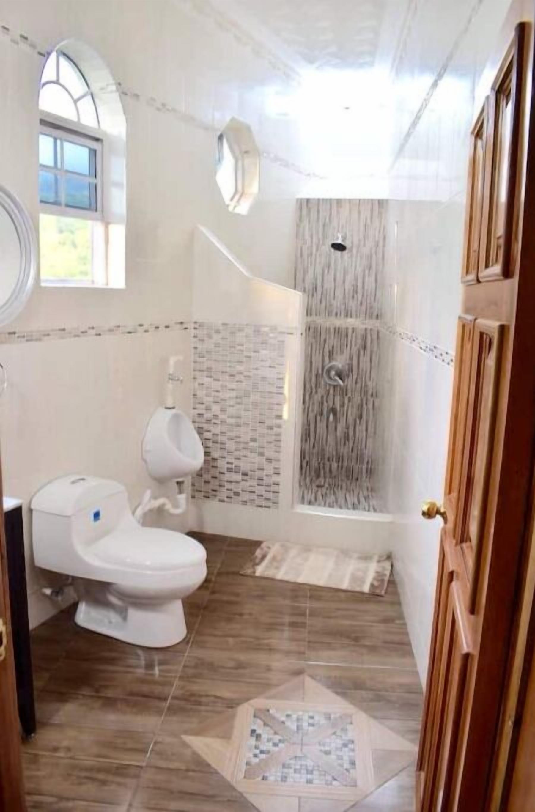 A bathroom with a toilet, urinal, shower, and tiled floor.