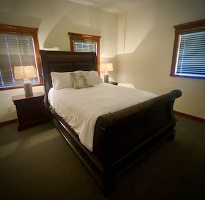 A bedroom with a large bed, two bedside tables, and a window with blinds. - Park Place (Darby)