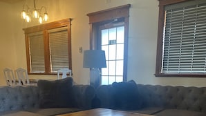 Ein Wohnzimmer mit einem großen Holztisch, einem grauen Sofa und einem Fenster mit Jalousien.