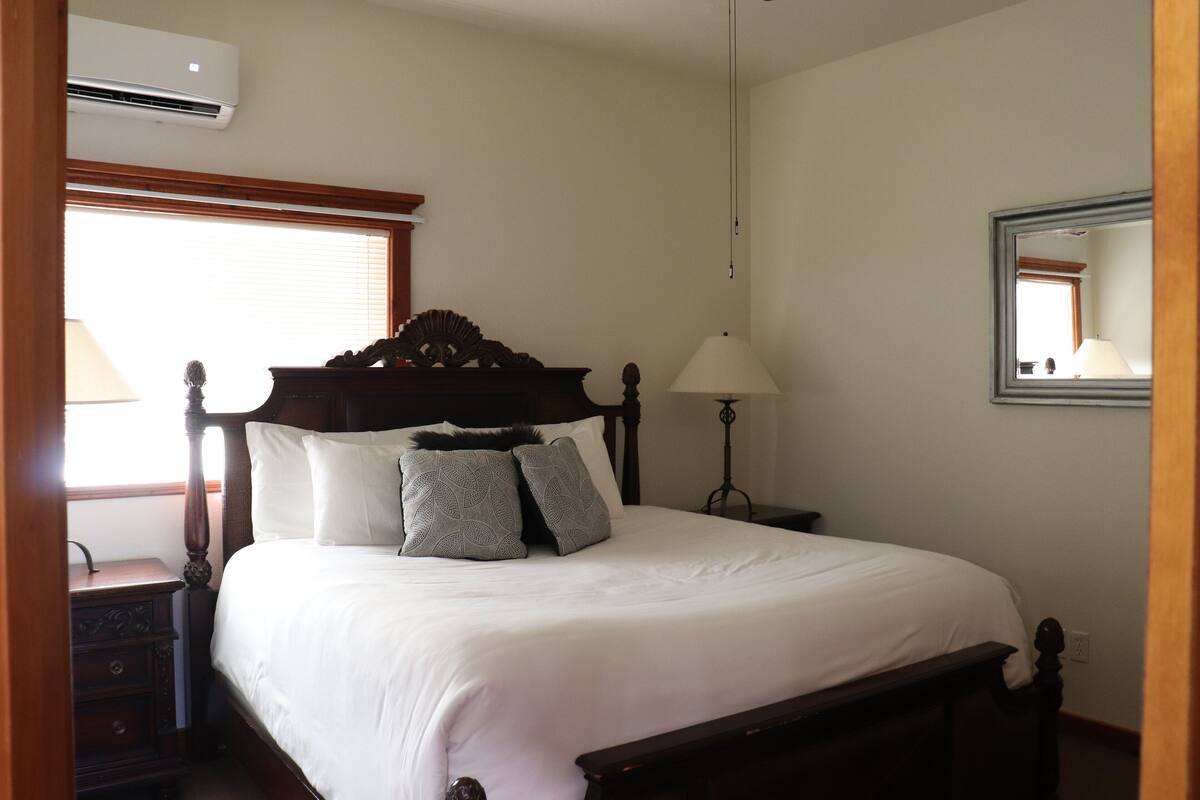 Una cama bien hecha con cabecera de madera, una lámpara de noche y un espejo en la pared.