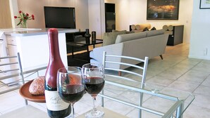 A modern living room with a dining area. There is a bottle of wine and two glasses on a table. A sofa and a TV are visible in the background. - South Palm Springs Resort-Style Getaway (Palm Springs)
