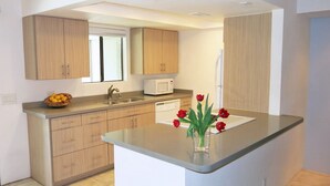 A modern kitchen with wooden cabinets, a built-in microwave, and a small island with a vase of red flowers. - South Palm Springs Resort-Style Getaway (Palm Springs)
