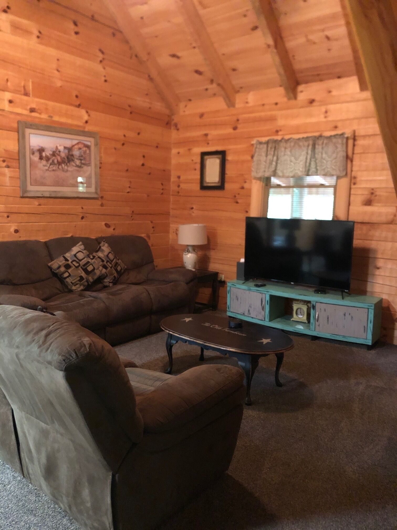 A cozy log cabin interior with a brown leather sofa, a small table, a television on a cabinet, and a framed picture on the wall.