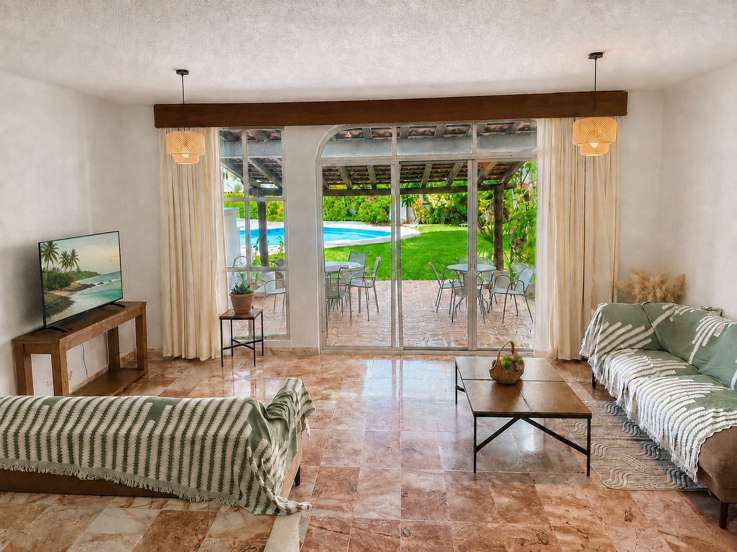 A living room with a TV, sofa, coffee table, and a view of a pool and garden.