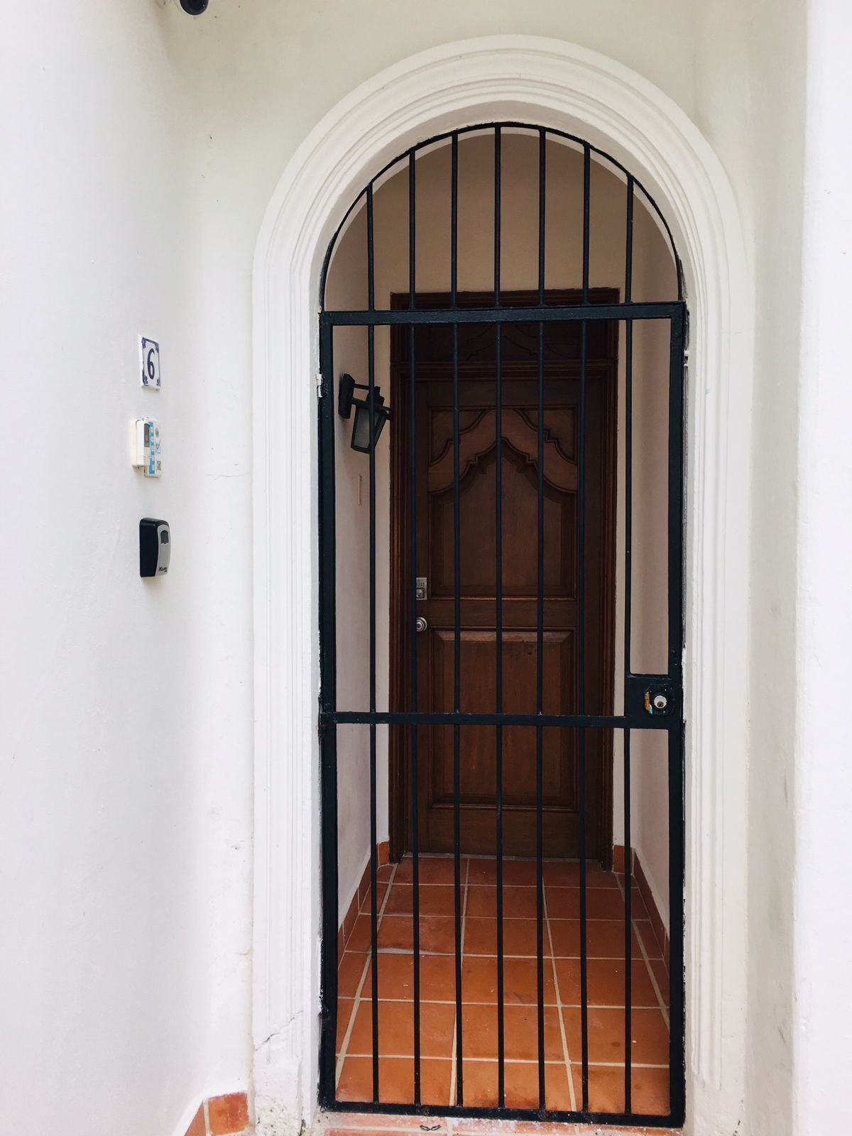 A white door with a black metal gate, a small light fixture, and a number '6' sign on the wall.