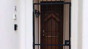 Una porta blanca amb una reixa de metall negra, un petit lluminari i un senyal amb el número 6 a la paret.