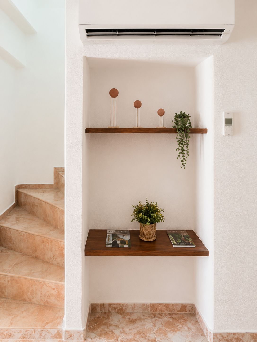 A staircase with a handrail, a wall-mounted air conditioning unit, and two wooden shelves with decorative items and a plant.