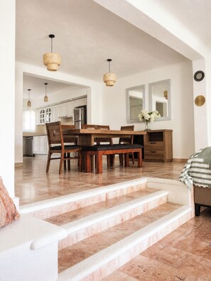A spacious living area with a dining table, chairs, and a staircase leading to an upper level.