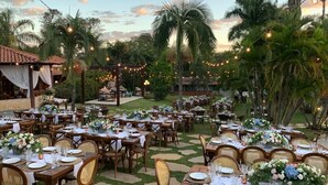 An outdoor dining area with tables set for a meal, surrounded by palm trees and string lights. - Estalagem Alter Real (Pirenópolis)