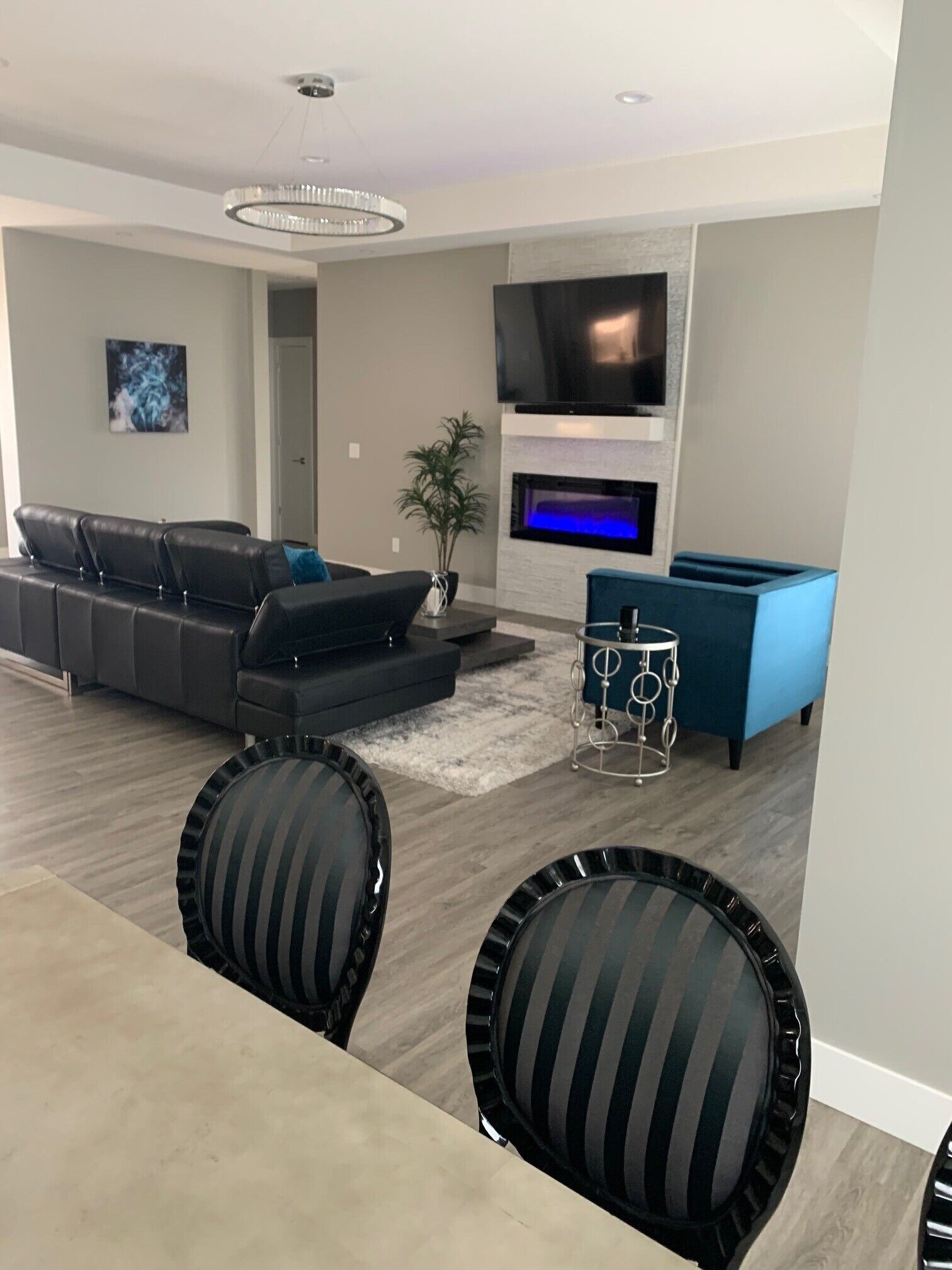 Un salon moderne avec un canapé d’angle, un téléviseur à écran plat fixé au-dessus d’une cheminée et un coin repas avec des chaises à rayures.