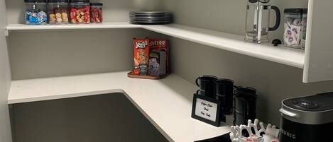 A kitchen with white cabinets, a coffee maker, and various food items on shelves.