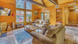 L’intérieur d’une cabane en rondins est aménagé avec un grand canapé, une table basse et une cheminée. Les murs sont en bois et le sol est en pierre.