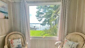 A room with two wicker chairs, each with a cushion featuring an anchor design. A large window offers a view of a lake and greenery. - Water Front Cottage (Edenton)