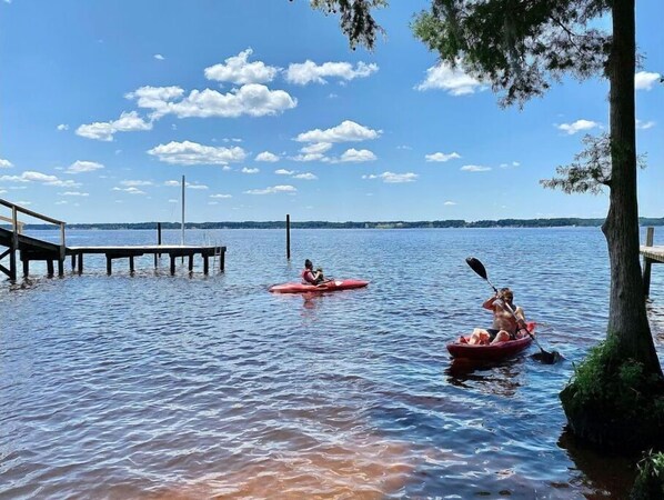 A calm lake with kayaks, a wooden dock, and a clear sky.