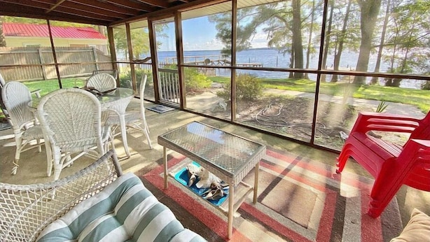 A covered outdoor seating area with wicker furniture, a glass table, and a view of the ocean. - Water Front Cottage (Edenton)