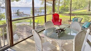 A covered outdoor area with a glass table and wicker chairs, overlooking a lake and dock. - Water Front Cottage (Edenton)