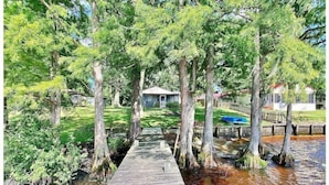 A wooden dock leading to a house surrounded by trees and a small body of water. - Water Front Cottage (Edenton)